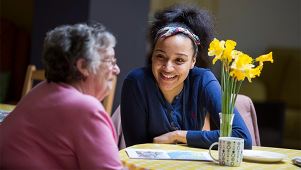 Two people smiling and engaging in conversation at a table, with a vase of daffodils.