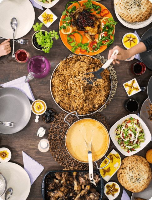 Image Description: A flat lay of traditional Arabic dishes on a table, with a traveler scooping biryani from a massive dish
