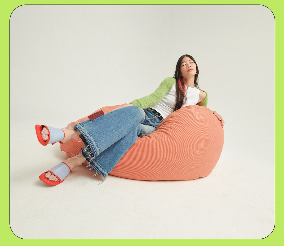 A girl with dark hair laying sideways on a peach squishy chair. 