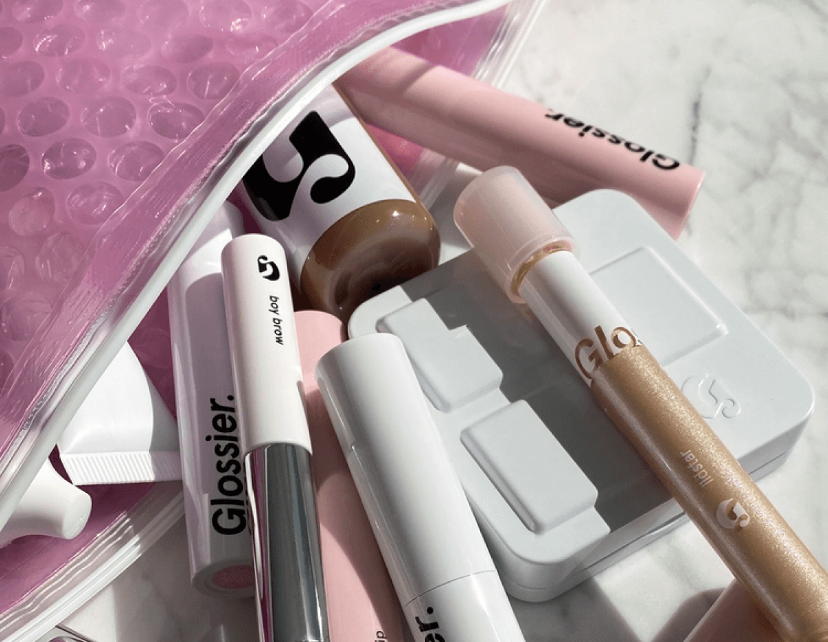 Various Glossier products spilling out of a pink Glossier pouch